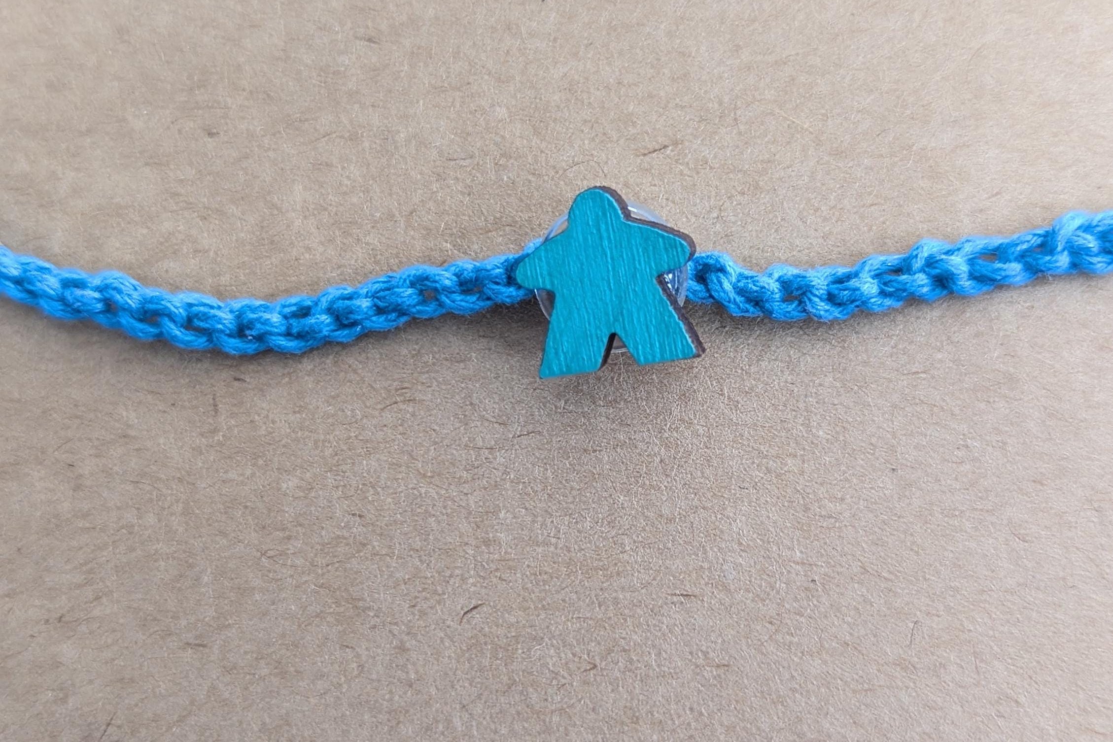 Blue braided bracelet with a blue meeple charm on a beige background