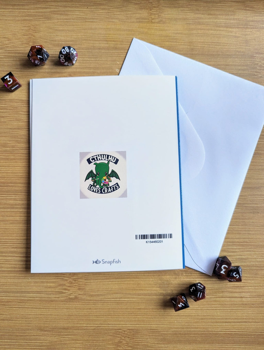 Card back with a cthulhu loves crafts logo on a wooden surface with dice around it
