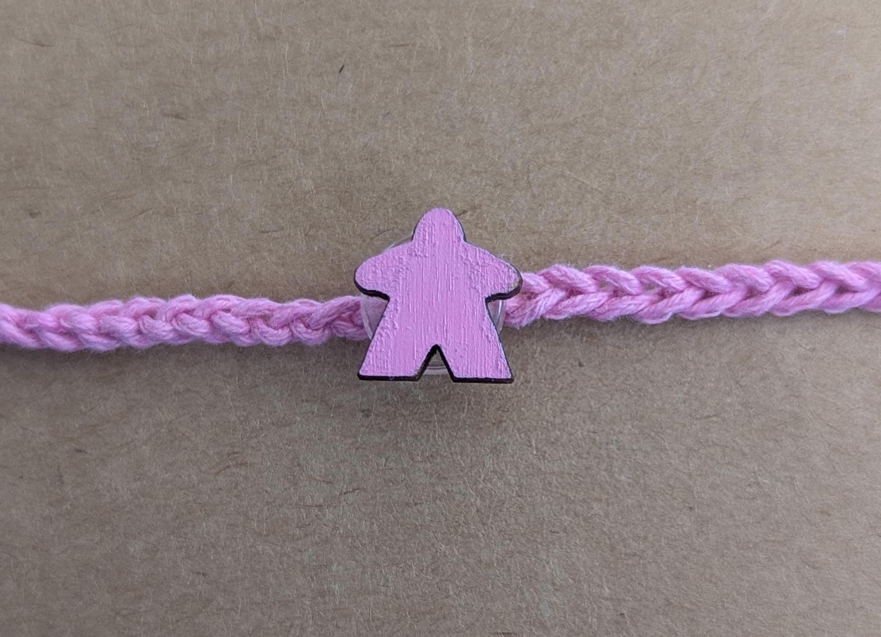 Pink braided bracelet with a matching meeple pink charm on a brown background