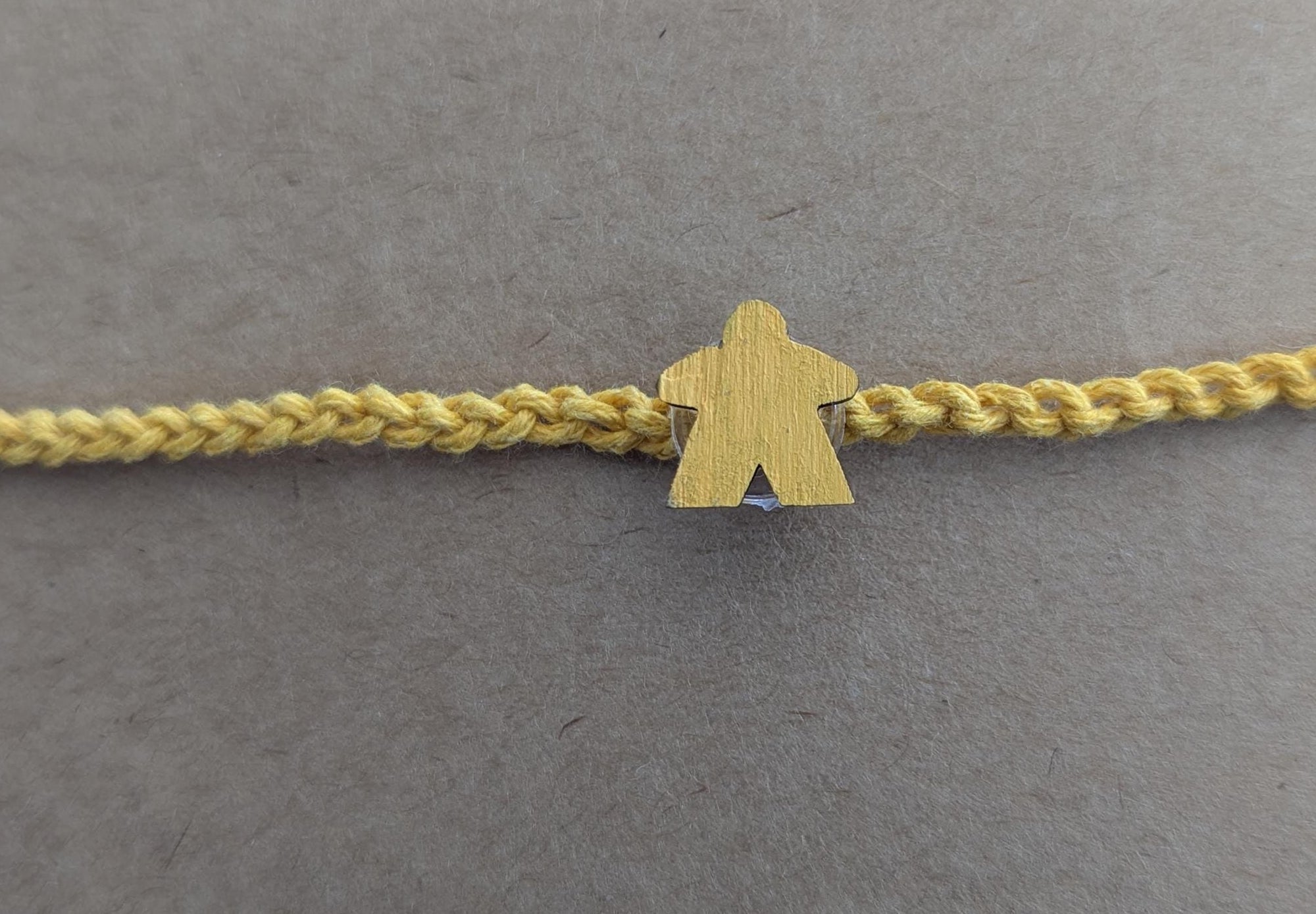 Yellow bracelet with a matching meeple charm on a beige background