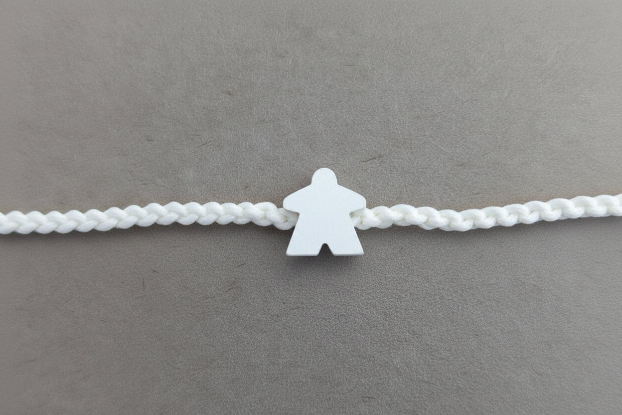 A white braided cord bracelet with a small white silhouette charm in the center, laid flat on a textured light gray surface.