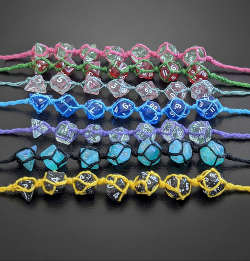 Seven sets of translucent polyhedral gaming dice made into macrame  bracelets arranged horizontally on a dark gray background. The sets include pink, green, light blue, purple, black, and yellow cords, with dice in clear, blue, green, red and black.