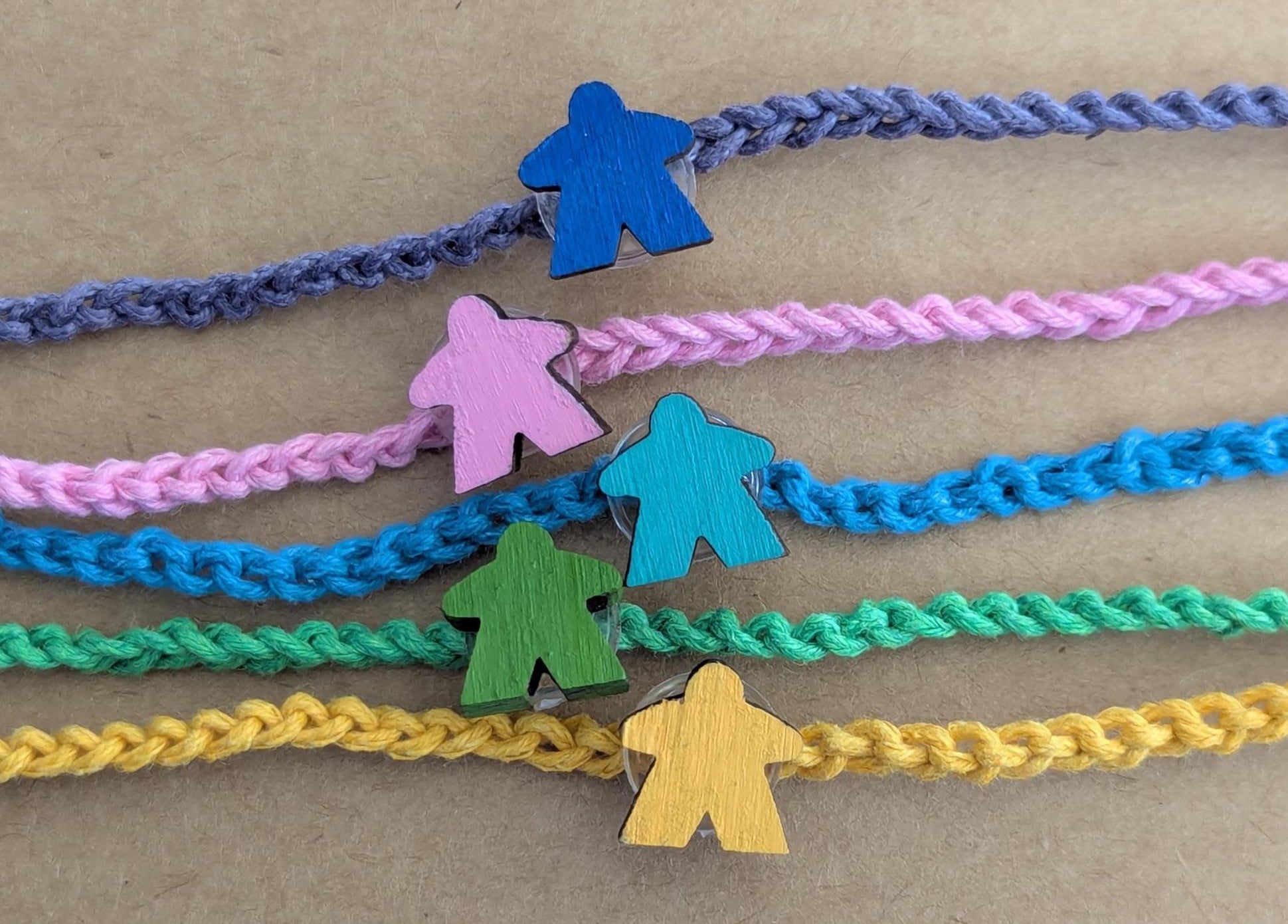 Colorful braided bracelets with meeple figures on a brown background