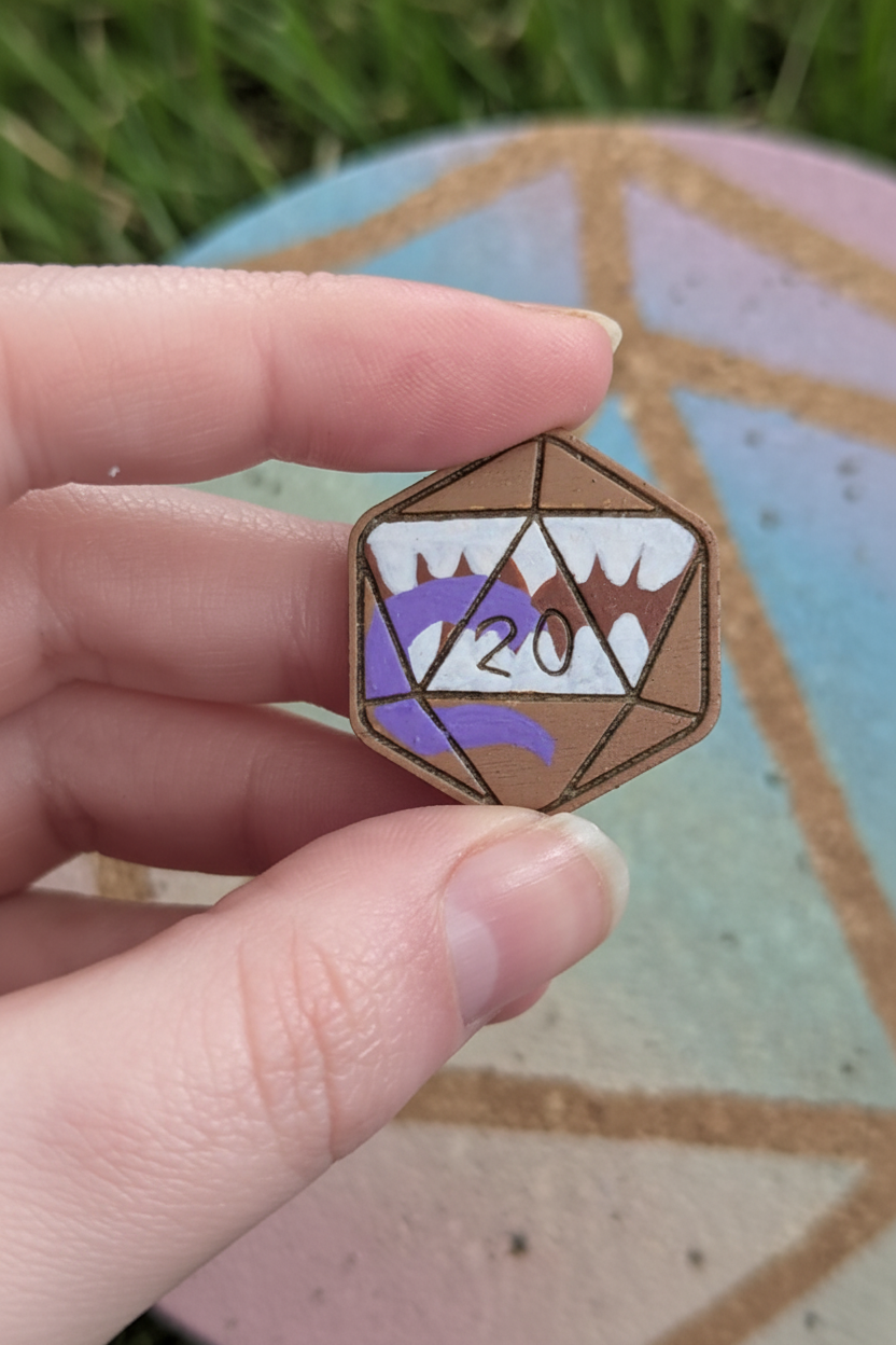 A hand holding a small mimic pin shaped like a 20-sided die, with white teeth and a purple tongue.