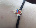 A close-up of a person's wrist wearing a black braided cord bracelet featuring a red and blue anatomical heart design.