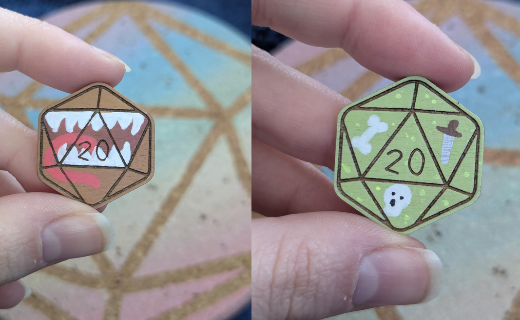 A side-by-side comparison of two hand-held pins shaped like a 20-sided d20 die. The left pin is painted as a mimic and the right pin is painted like a Gelatinous cube.